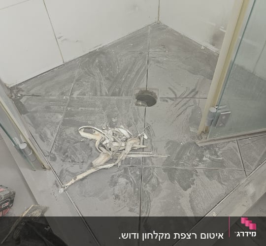 רצפת מקלחת עם אריחים שבורים וחור ניקוז חשוף